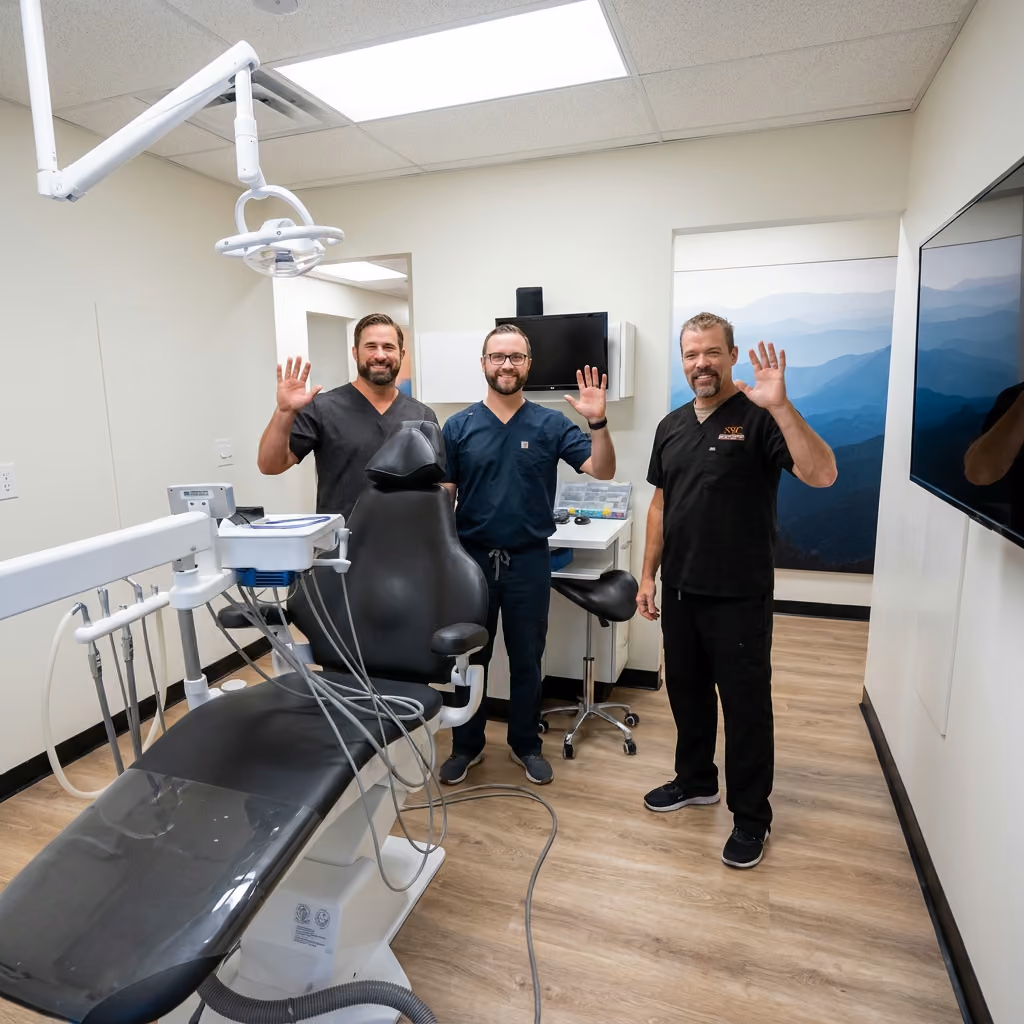 Three smiling dentists, Dr. Curtis, Dr. Anderson, and Dr. Brimhall, wave in a modern dental treatment room.