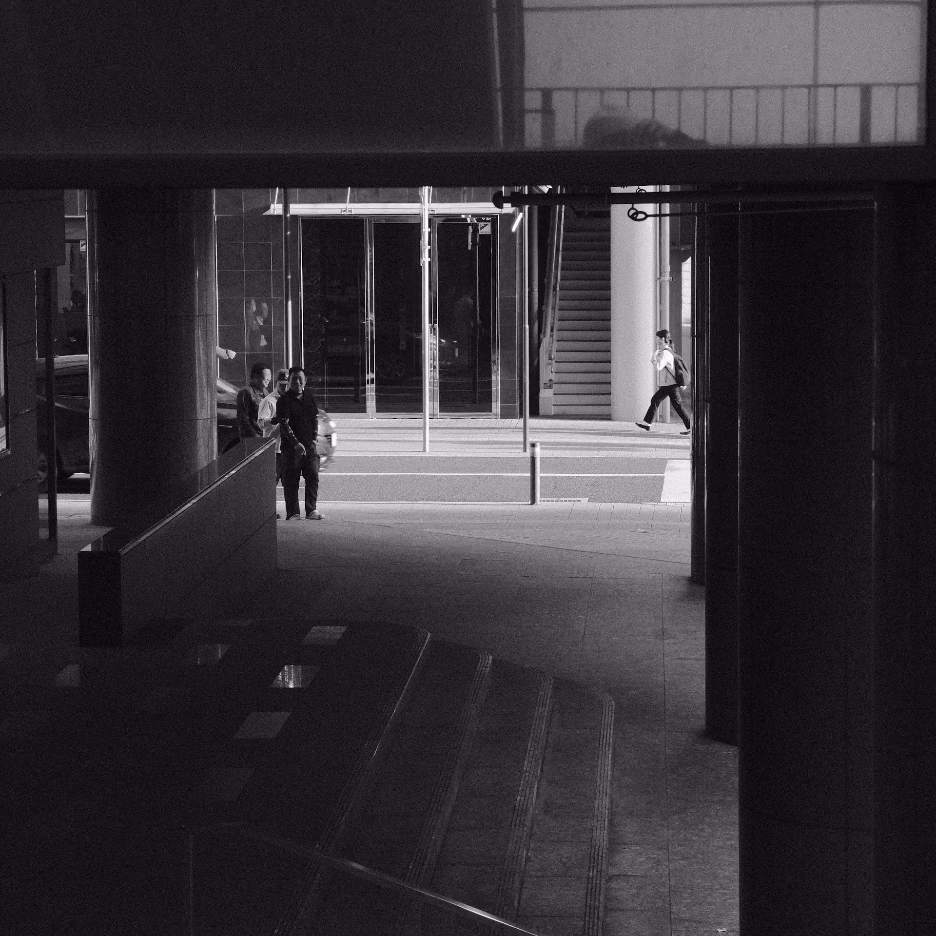 Composición arquitectónica en blanco y negro que encuadra desde la sombra el paso de personas en una calle iluminada. Representa el enfoque en la intención de compra y el funnel de conversión.