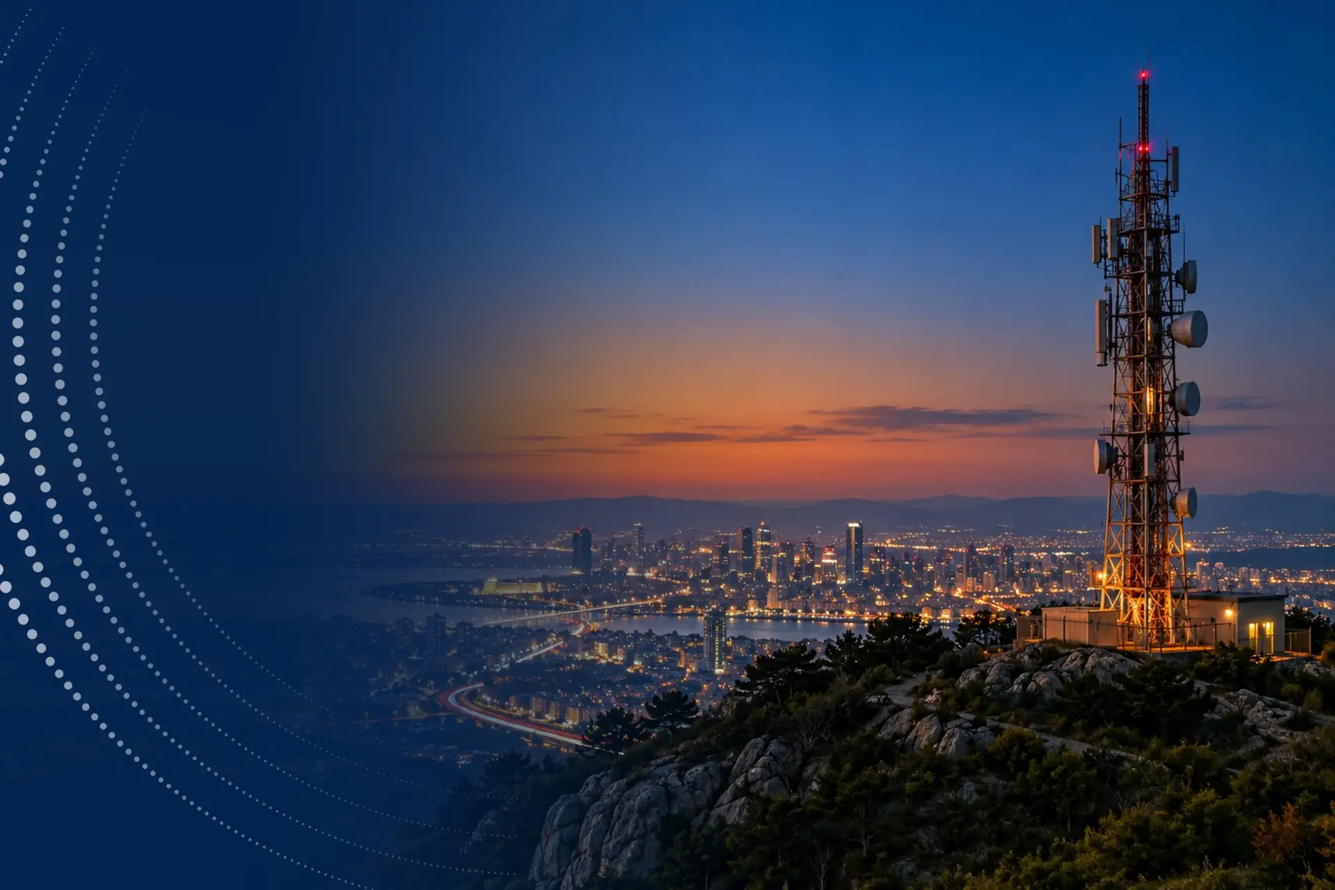 A telecommunications tower above a city lit up at dusk.