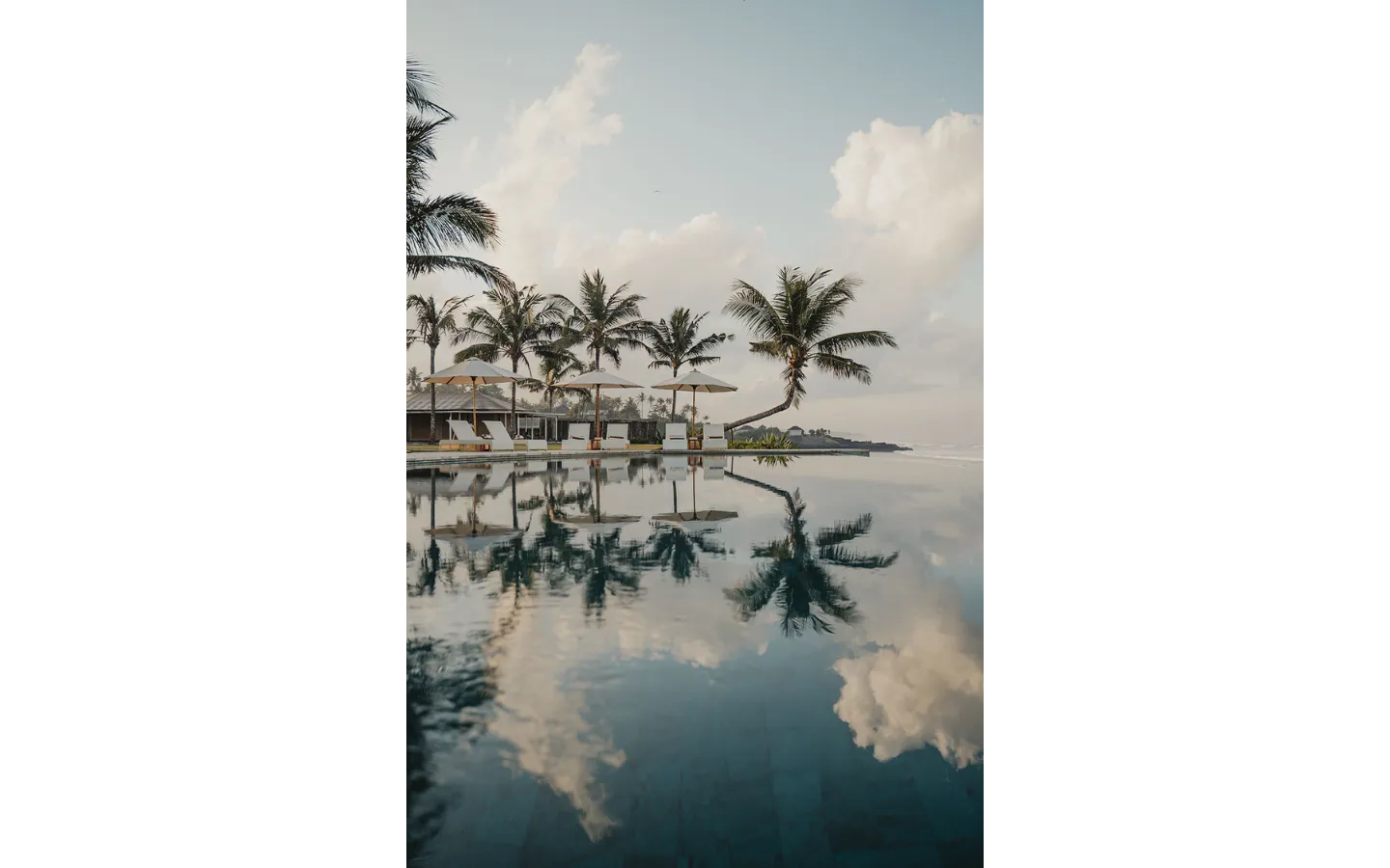 Infinity pool reflecting palm trees against a cloudy sky