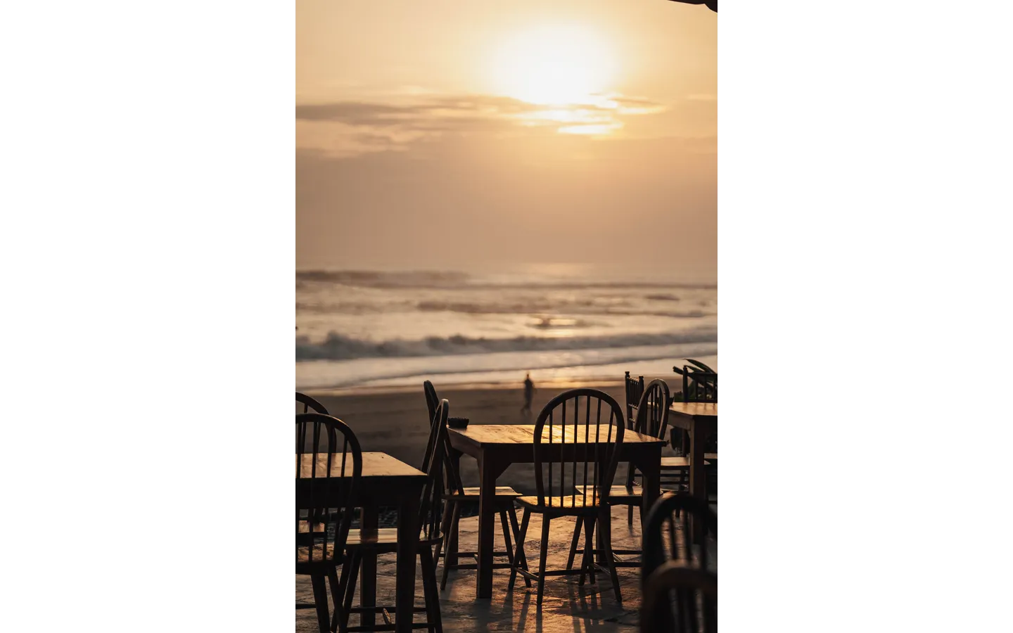 Silhouette of empty beachfront dining tables and chairs at sunset