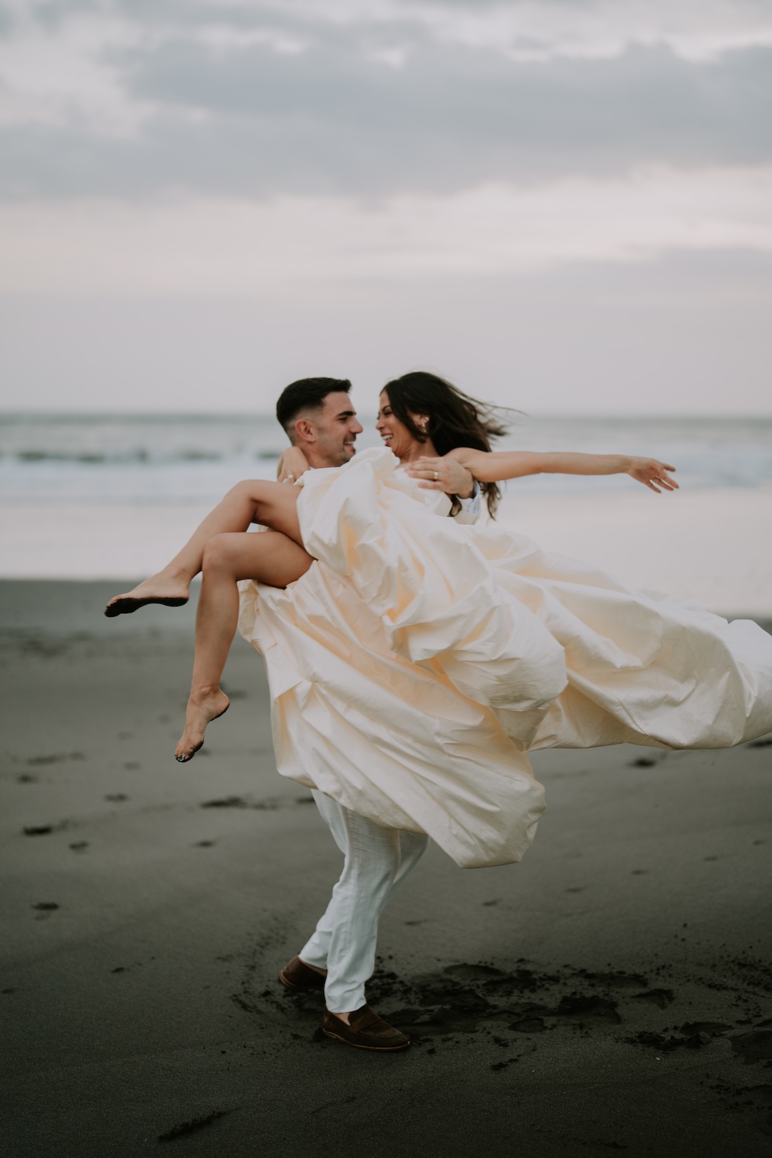 Groom carrying his laughing bride along the beach