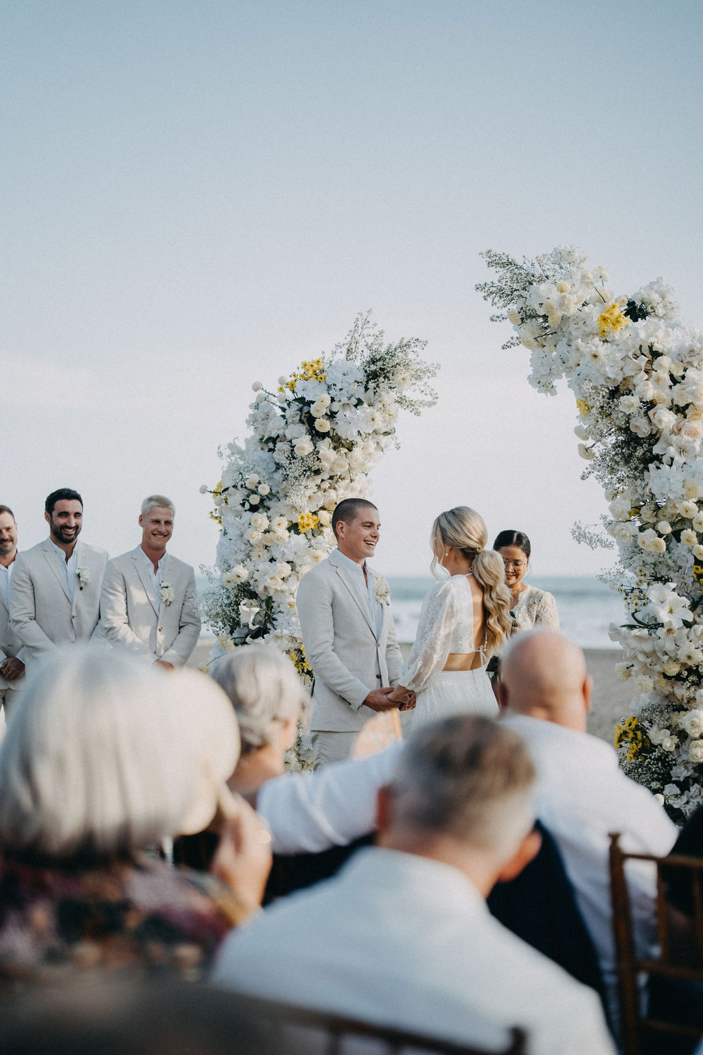 Bride and groom holding hands during their ceremony under a floral arch