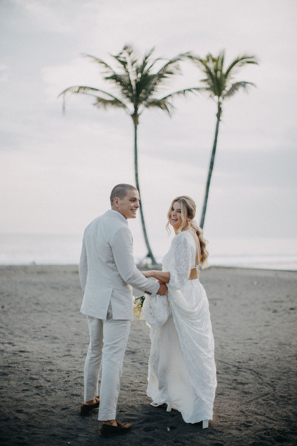 Bride and groom holding hands on the beach in front of palm trees
