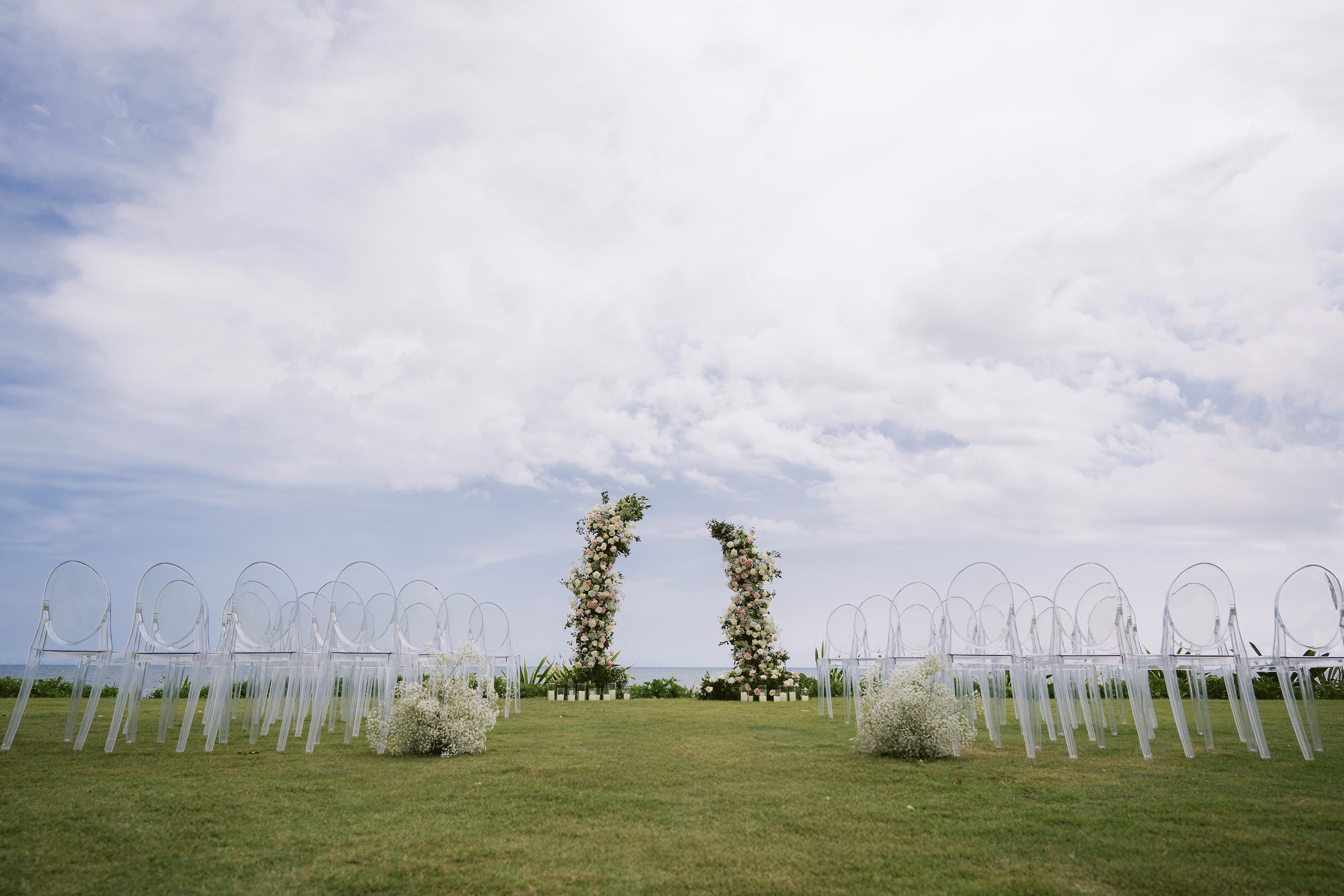 Clear ghost chairs and a floral arch set up on the lawn for a wedding ceremony