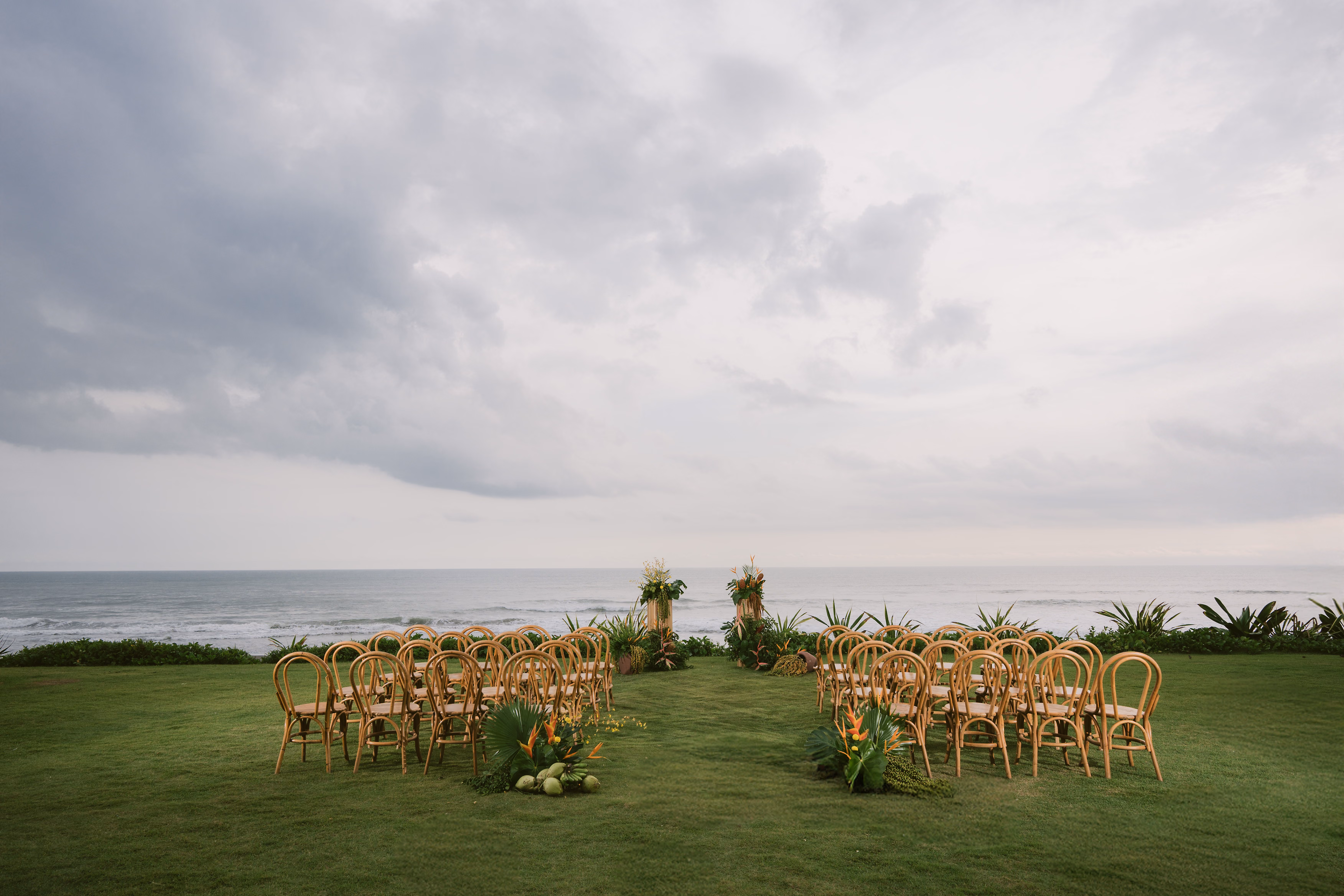Rattan chairs arranged in rows on the oceanfront lawn for a wedding ceremony