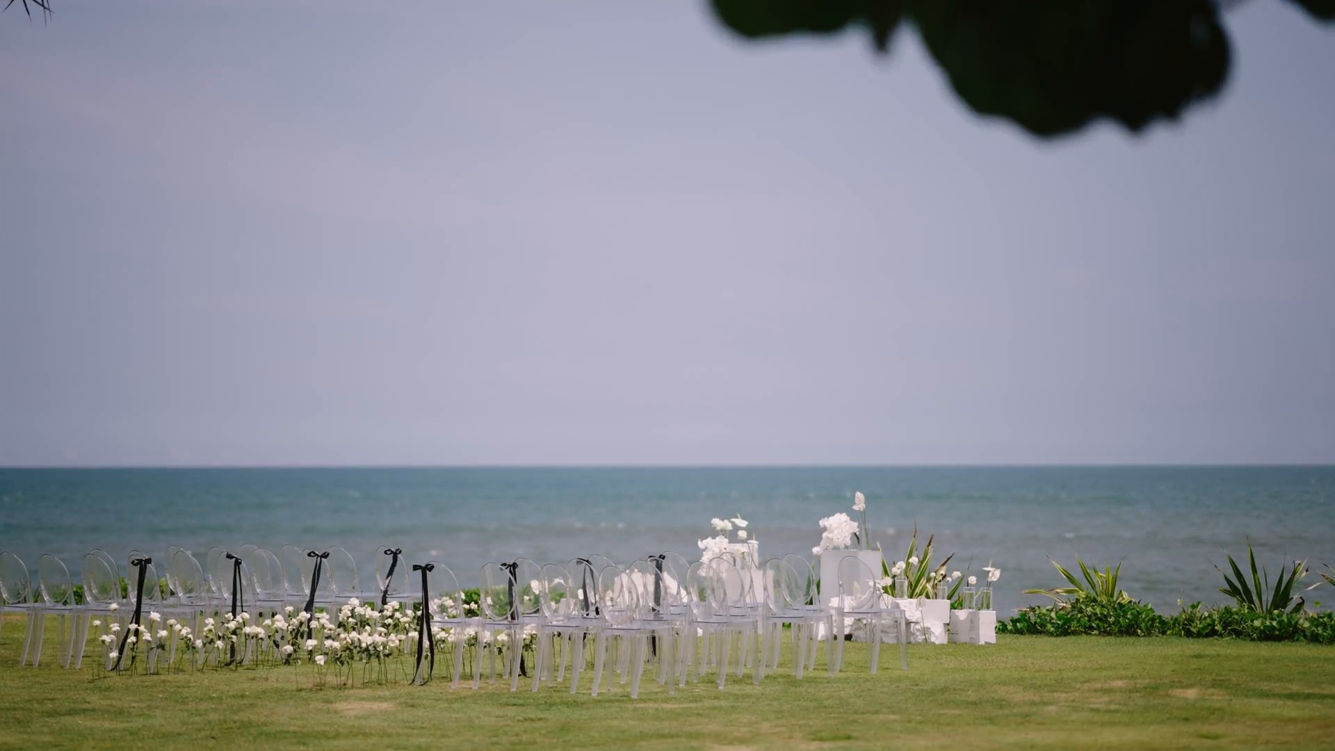 Aisle of white ceremony chairs and a floral arch facing the ocean for a wedding