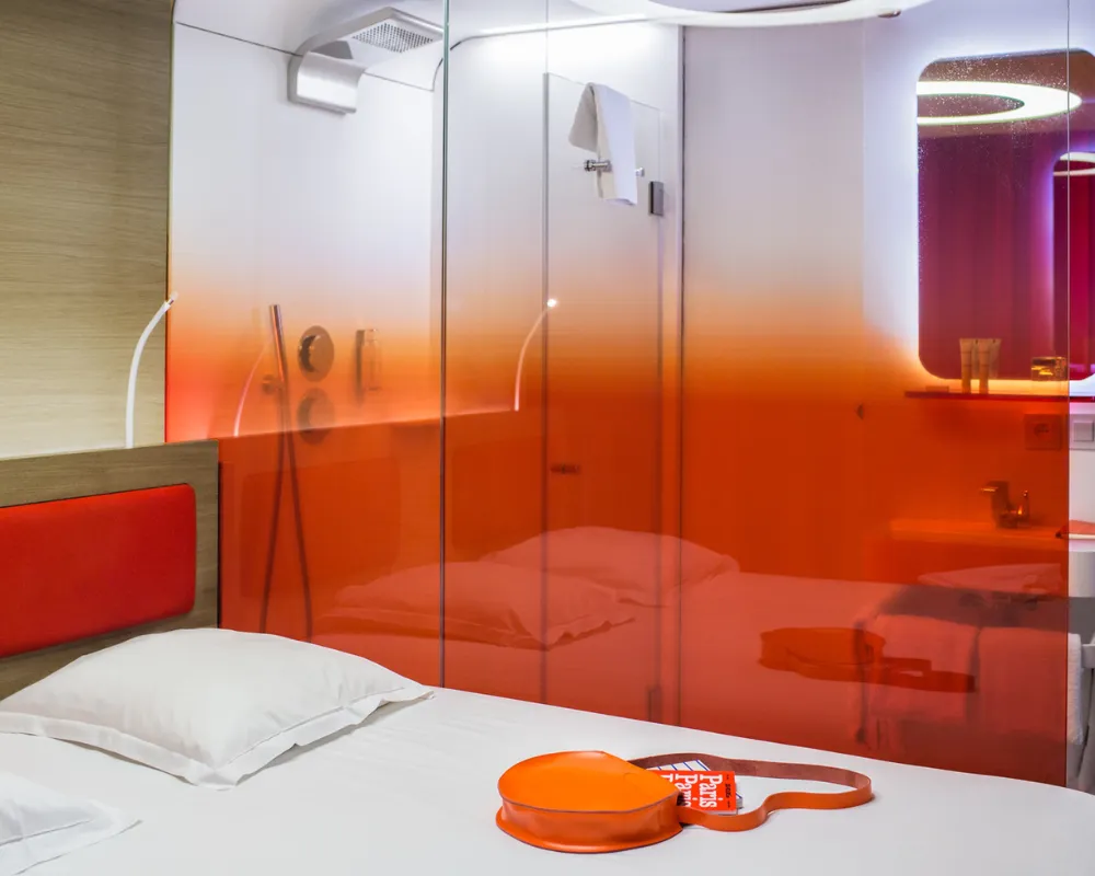 Lit et paroi vitrée orange de la chambre Odyssey, hôtel capsule à Paris 1er