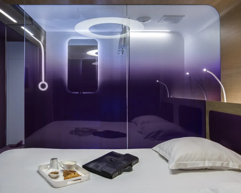 Lit face à la paroi vitrée violette lumineuse, hôtel capsule à Paris 1er