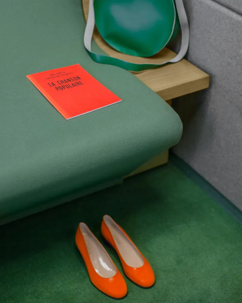 Ballerines orange et livre rouge sur la banquette, hôtel capsule à Paris 1er