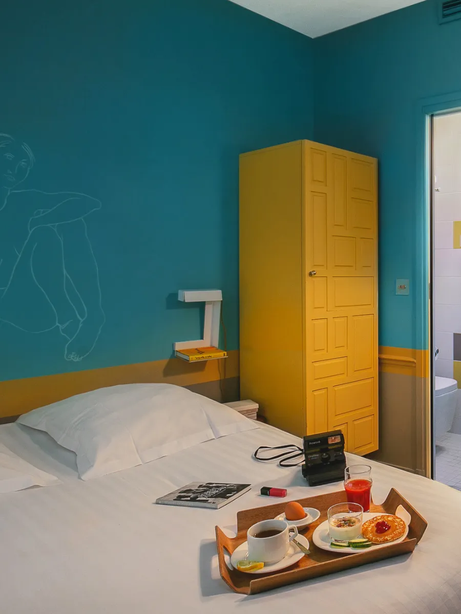 Chambre bleu canard avec armoire jaune et petit-déjeuner au lit, l'une des 26 chambres uniques de l'Hôtel Crayon, Paris