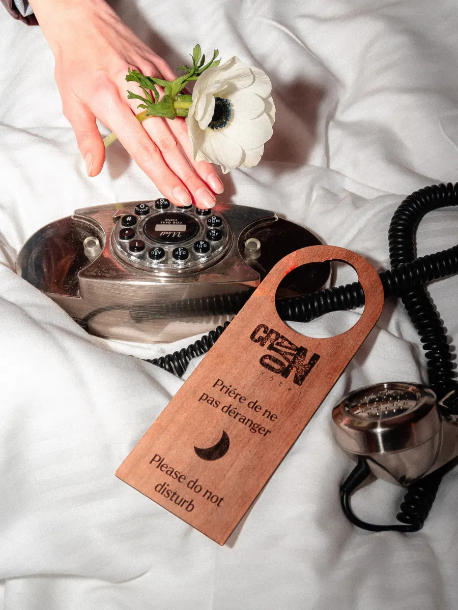 Accroche-porte en bois Crayon, téléphone vintage et fleur blanche sur le lit, Hôtel Crayon écoresponsable à Paris