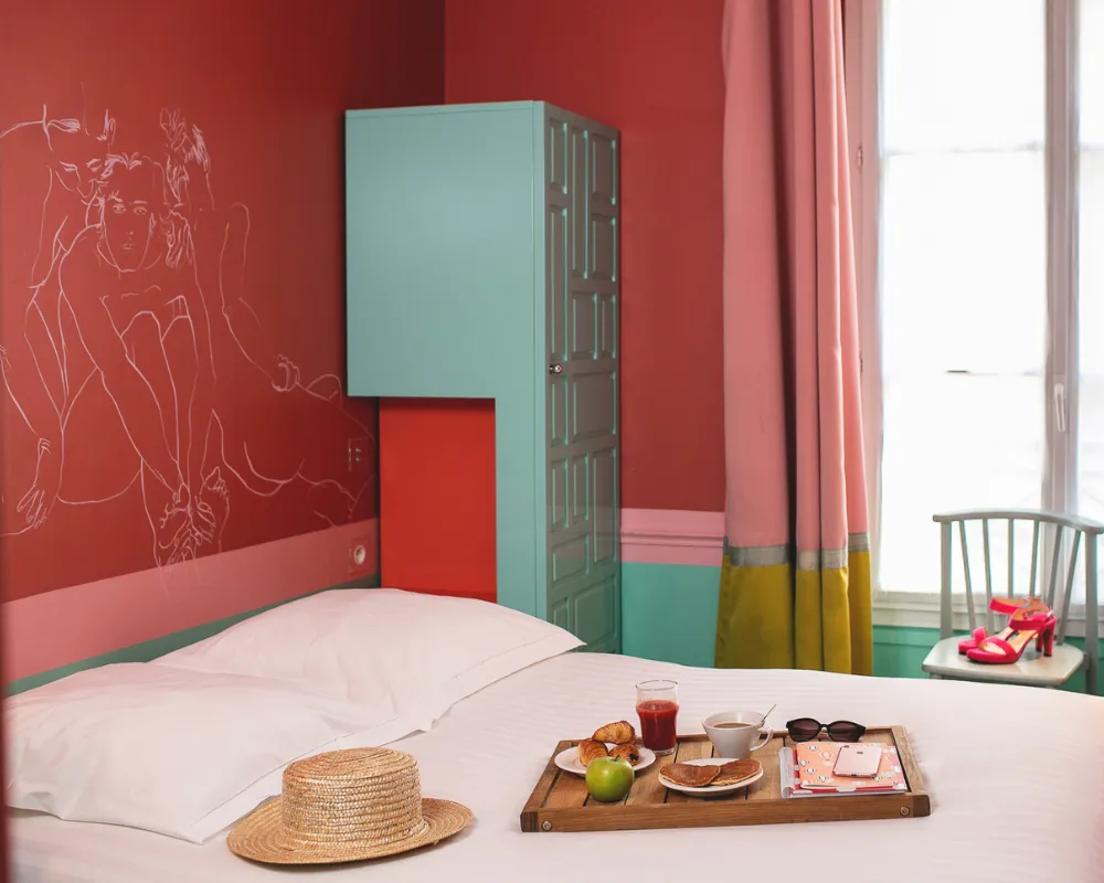 Chambre Singulière de l'Hôtel Crayon à Paris 1er, lit avec chapeau de paille et plateau petit-déjeuner près de la fenêtre