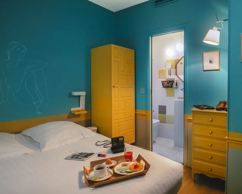 Chambre bleue de l'Hôtel Crayon à Paris 1er : commode jaune, armoire assortie et petit-déjeuner servi au lit