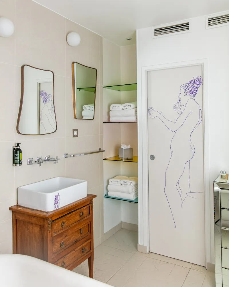 Salle de bain de la Suite Junior à l'Hôtel Crayon, Paris 1er : vasque sur commode ancienne et porte dessinée à la main