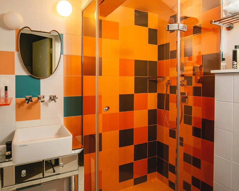 Douche carrelée orange et noir en damier et vasque blanche dans une salle de bain de l'Hôtel Crayon, Paris 1er