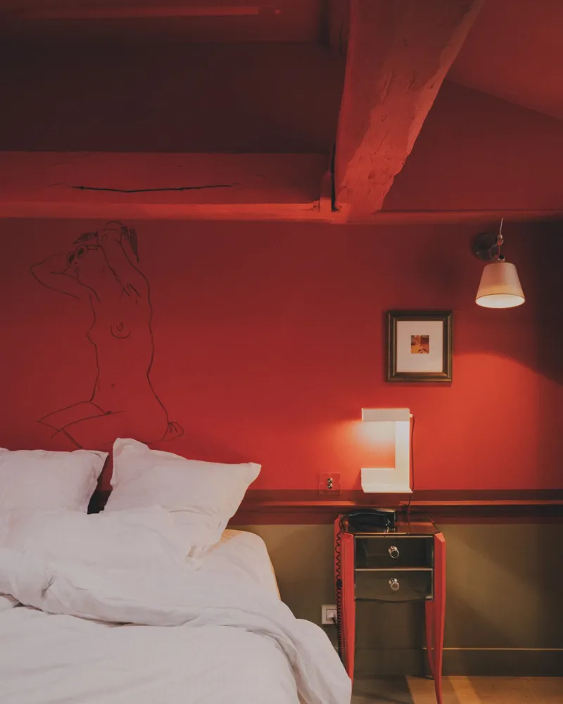 Chambre rouge de l'Hôtel Crayon à Paris 1er avec poutres apparentes, lit double et dessin mural au trait