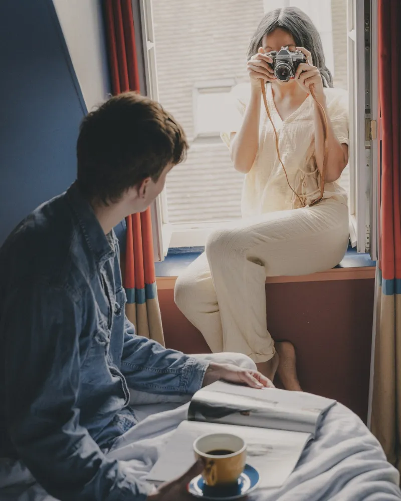 Couple dans une chambre de l'Hôtel Crayon à Paris, la femme photographie depuis le rebord de la fenêtre