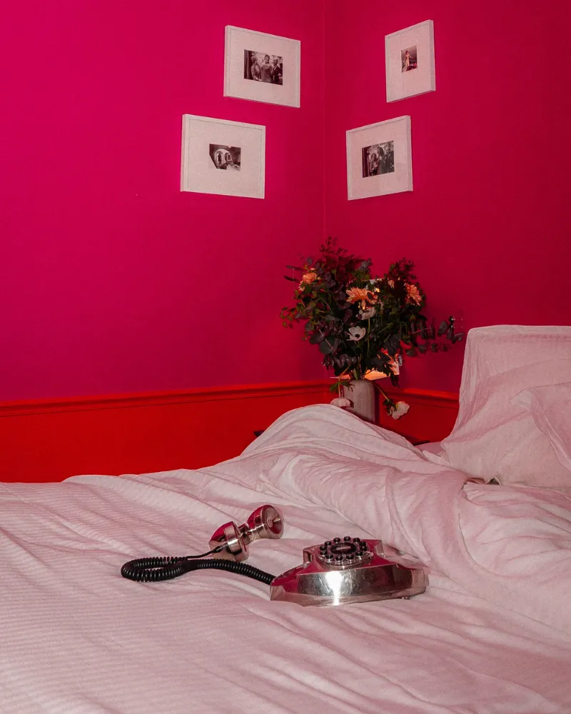 Lit défait dans une chambre rose fuchsia de l'Hôtel Crayon à Paris 1er, bouquet de fleurs et cadres photo