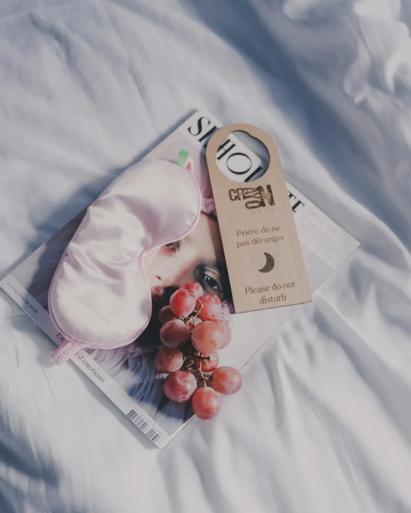 Masque de sommeil, accroche-porte Crayon et raisins sur les draps blancs d'une chambre de l'Hôtel Crayon à Paris