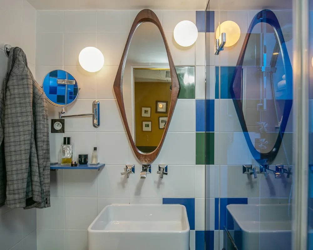 Salle de bain à deux vasques, carrelage bleu et miroirs en bois dans une chambre de l'Hôtel Crayon à Paris 1er