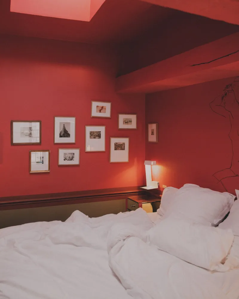 Chambre rouge mansardée de l'Hôtel Crayon à Paris 1er, lit double défait et mur de cadres photo