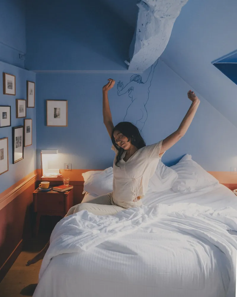 Cliente s'étirant au réveil dans une chambre mansardée bleue de l'Hôtel Crayon à Paris 1er