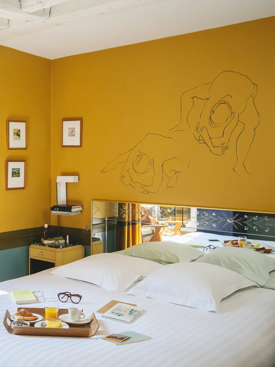 Chambre Insolite Double de l'Hôtel Crayon à Paris 1er, murs jaune moutarde dessinés et plateau petit-déjeuner sur le lit