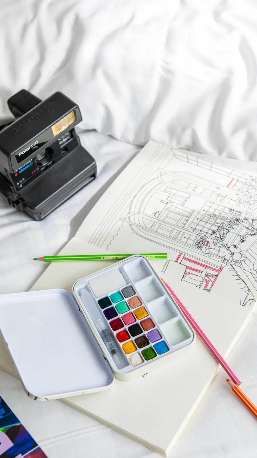 Appareil photo instantané, aquarelles et carnet de croquis sur un lit de l'Hôtel Crayon, hôtel d'artiste à Paris