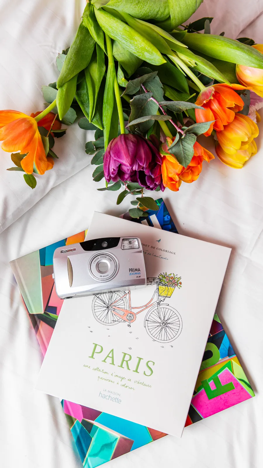 Tulipes, livre sur Paris et appareil photo posés sur un lit de l'Hôtel Crayon, boutique-hôtel du 1er arrondissement