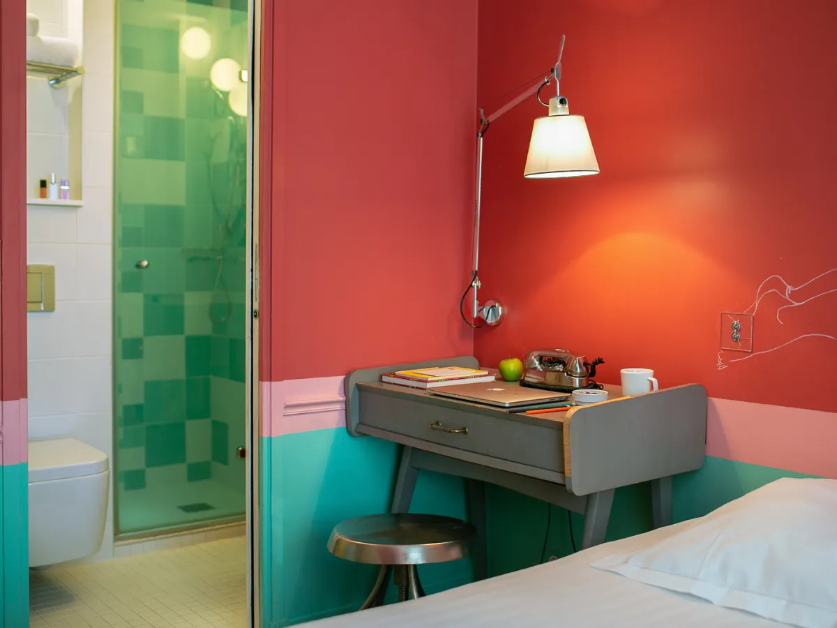 Red and turquoise room at the Hôtel Crayon in Paris 1st arrondissement with a vintage desk, lamp, and green tiled shower