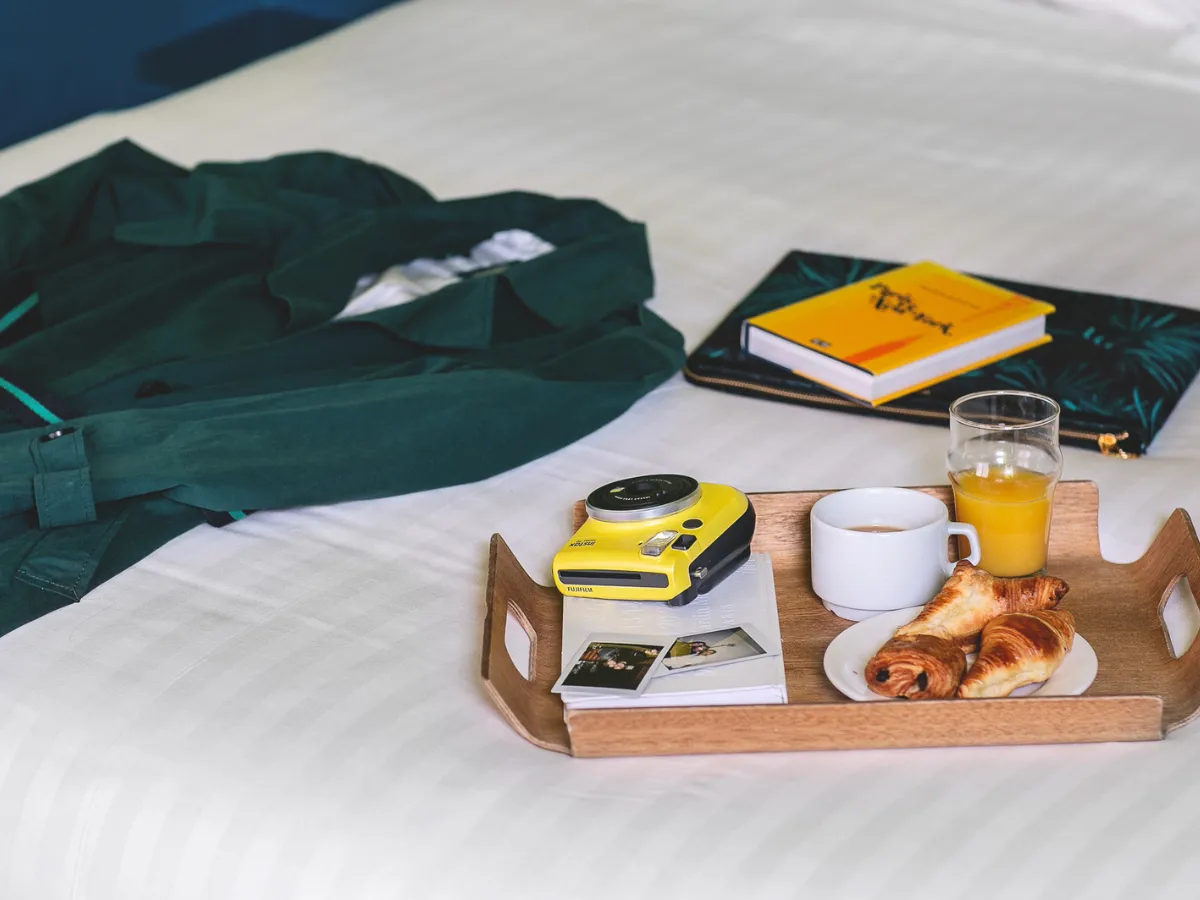 Breakfast tray, yellow camera, and a book on a bed at Hôtel Crayon, an arty hotel in Paris