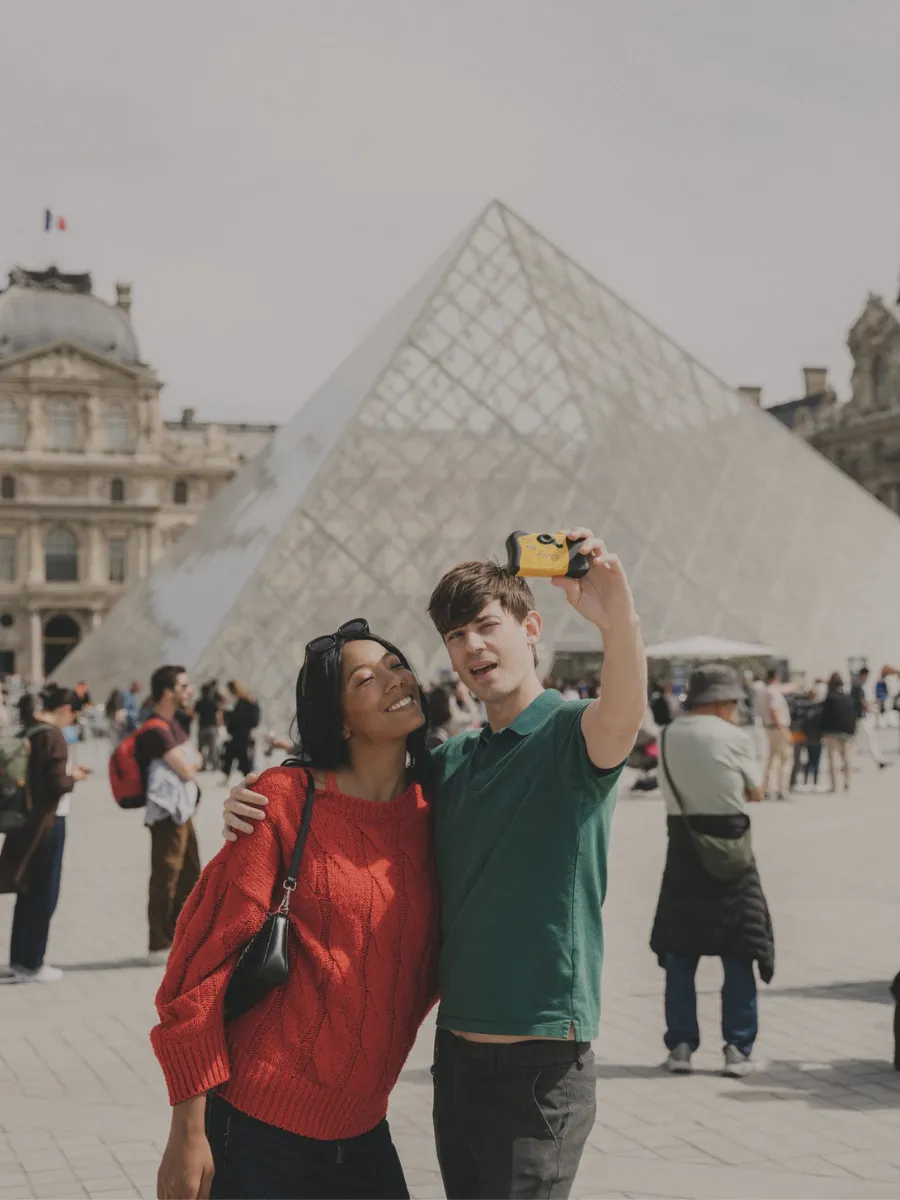 Couple taking a selfie in front of the Louvre Museum pyramid, just a stone's throw from Hôtel Crayon in Paris