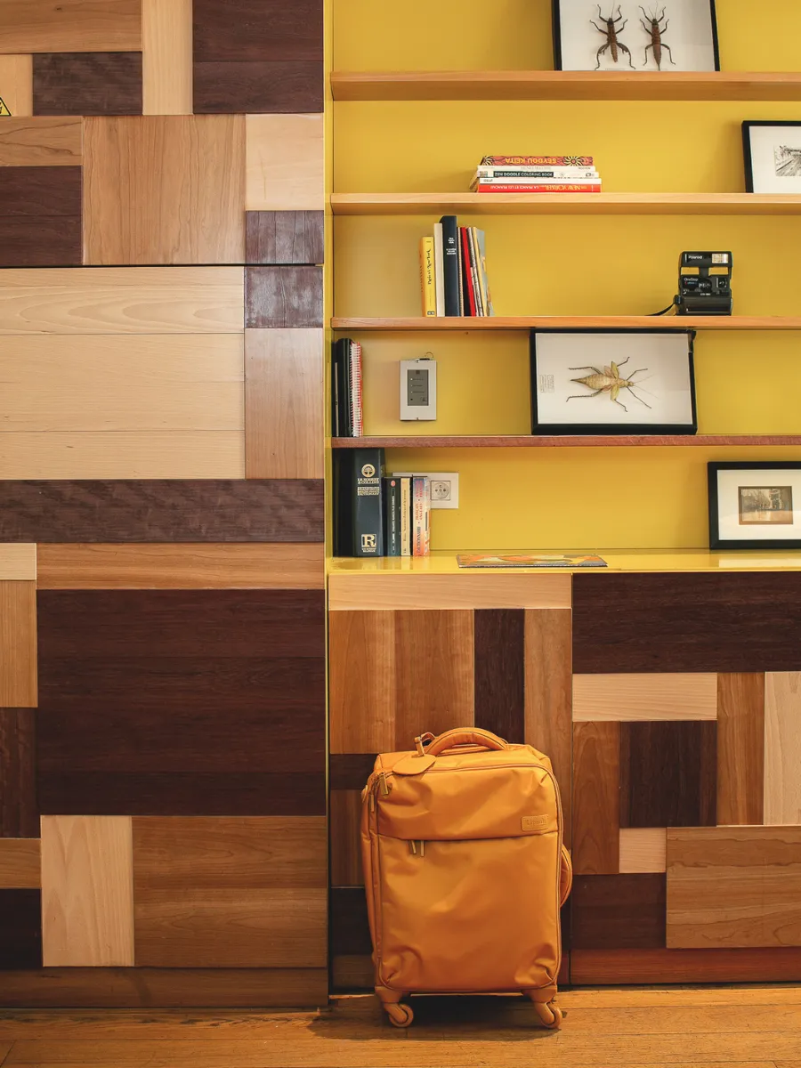 Yellow suitcase in front of the bookcase and colorful woodwork at the reception of Hôtel Crayon, Paris 1st arrondissement