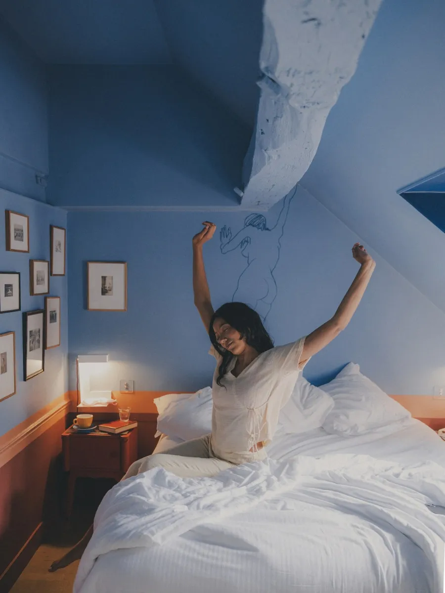 Guest waking up in a blue attic room decorated with picture frames at Hôtel Crayon, Paris 1st arrondissement