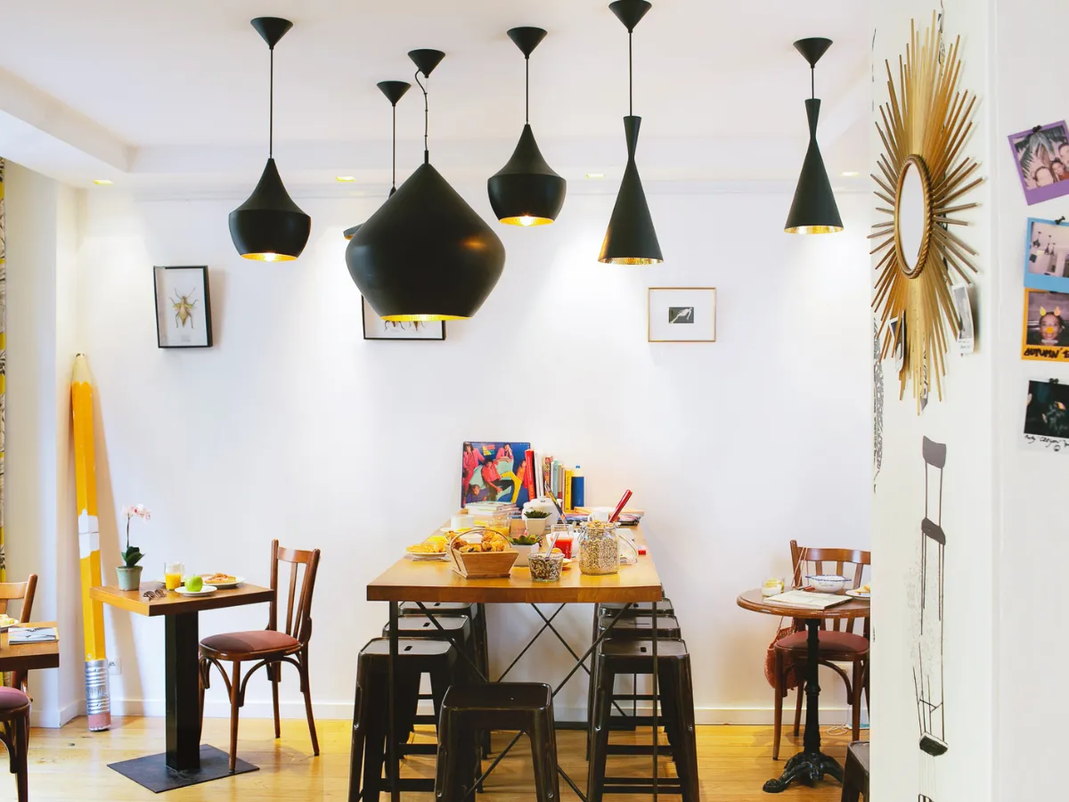 Breakfast room at the Hôtel Crayon in Paris 1st arrondissement: black pendant lights, wooden tables, and a gold sunburst mirror