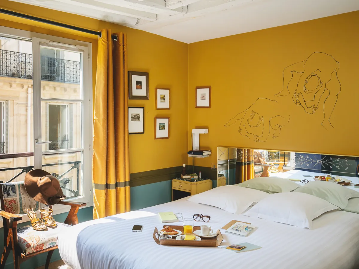 Mustard yellow room with line-art wall drawings and a street-facing window at Hôtel Crayon, Paris 1st Louvre
