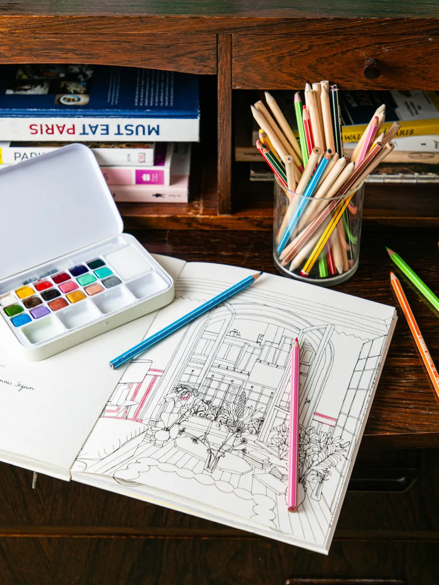 Aquarelles, crayons de couleur et carnet de dessin sur un bureau vintage de l'Hôtel Crayon, hôtel d'artiste à Paris