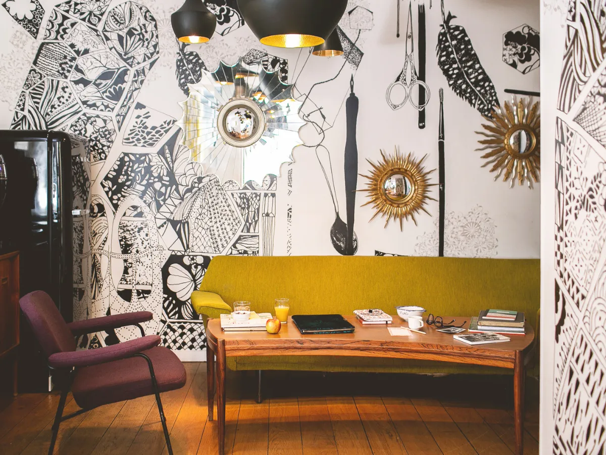 Arty lounge at Hôtel Crayon in Paris' 1st arrondissement, featuring black and white illustrated walls, gold mirrors, and a mustard-colored bench.