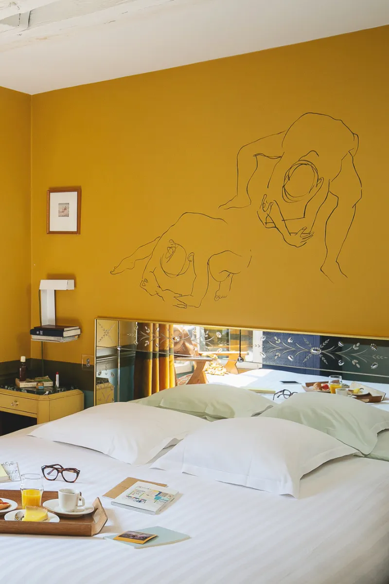 Chambre jaune moutarde de l'Hôtel Crayon à Paris 1er avec dessin mural et petit-déjeuner au lit