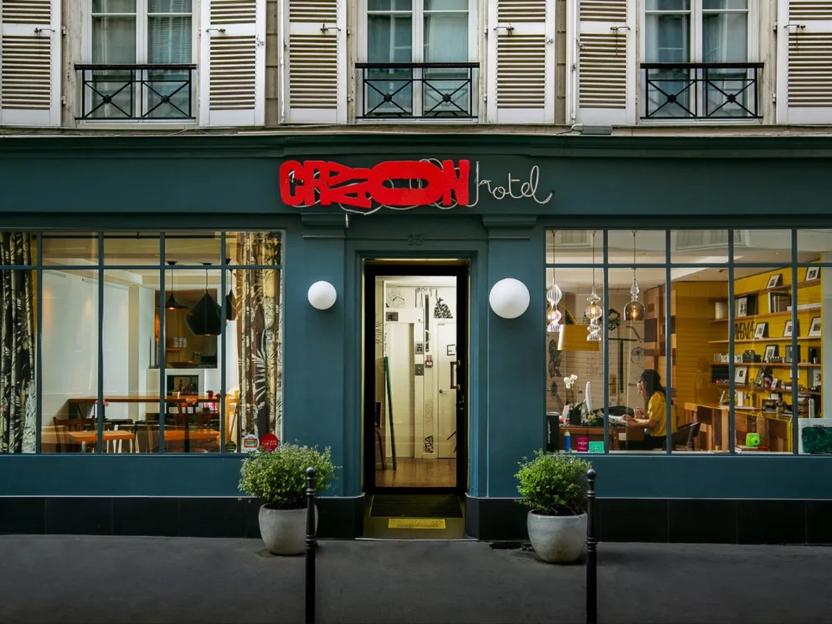 Façade de l'Hôtel Crayon à Paris 1er avec ses vitrines éclairées, son enseigne néon et ses volets blancs