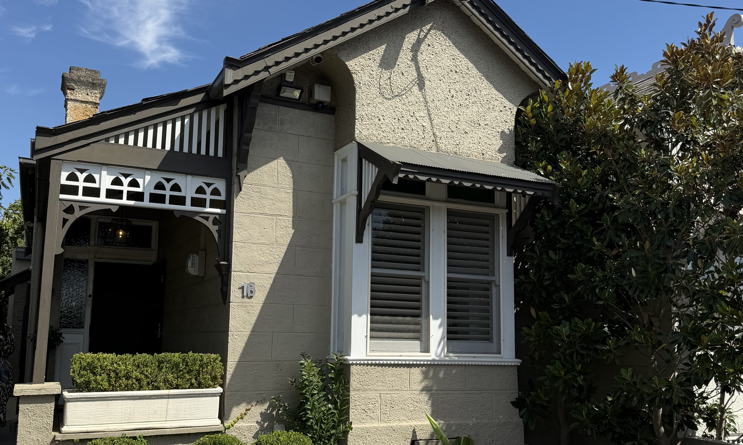Front of a rendered period home with a bay window and verandah