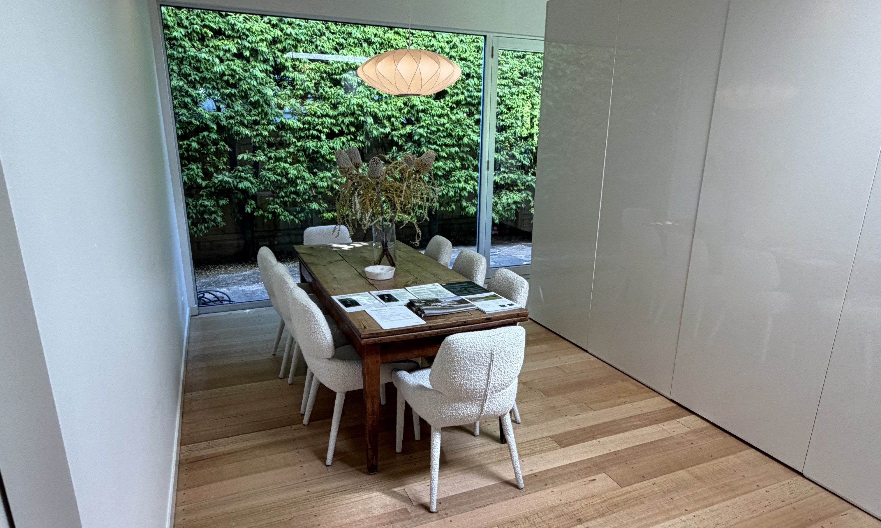 Dining table beside full-height glass onto a hedged courtyard