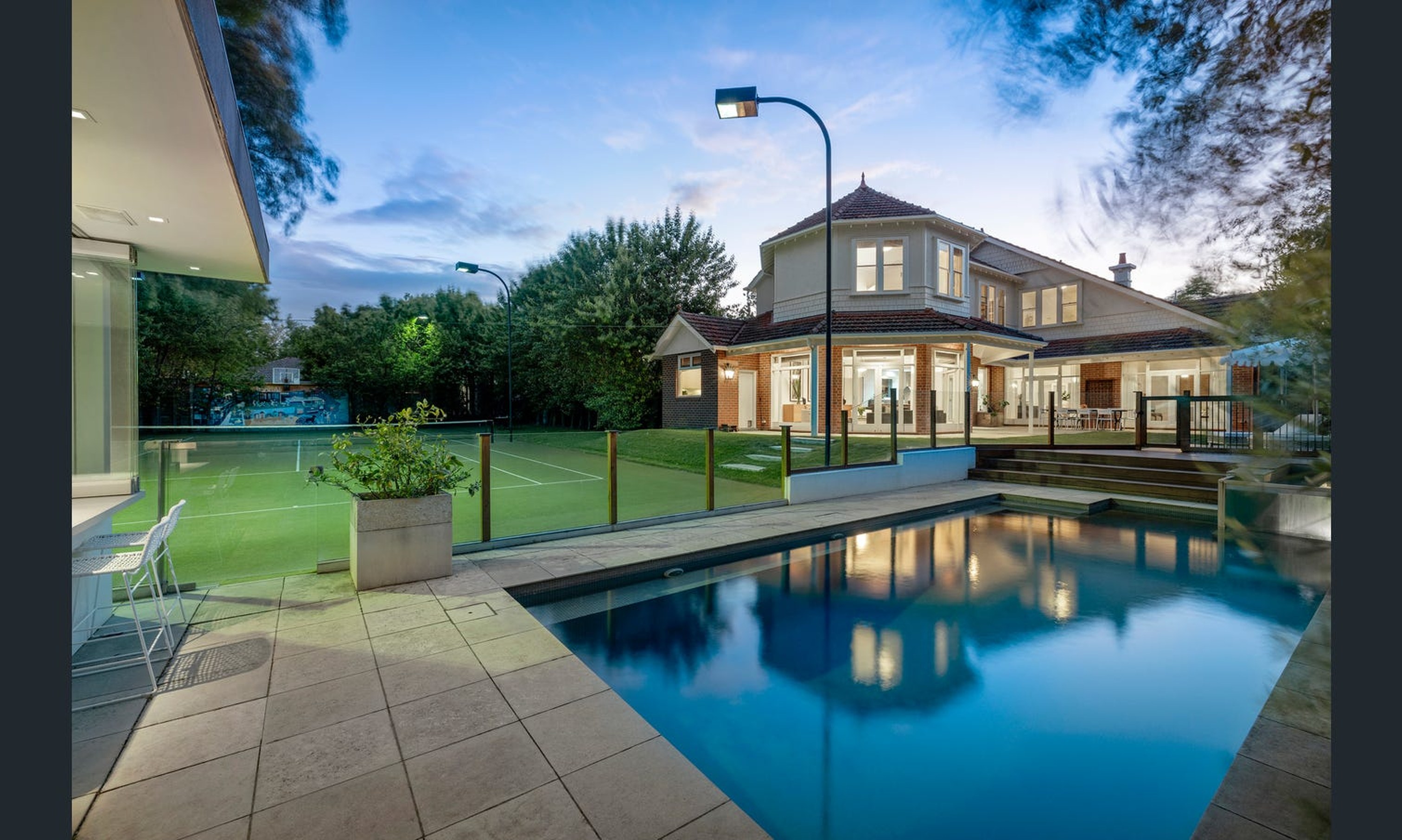 Period home lit at dusk beside a pool and lawn
