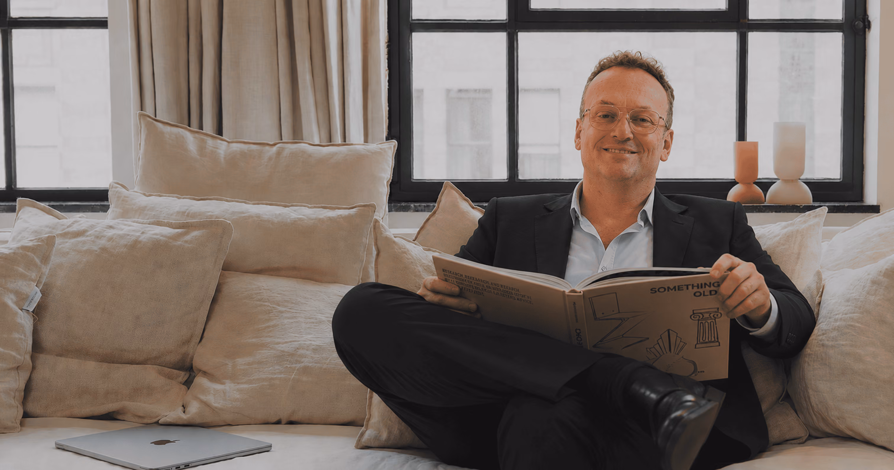 Man in suit with glasses sitting on couch reading a book titled Something Old.