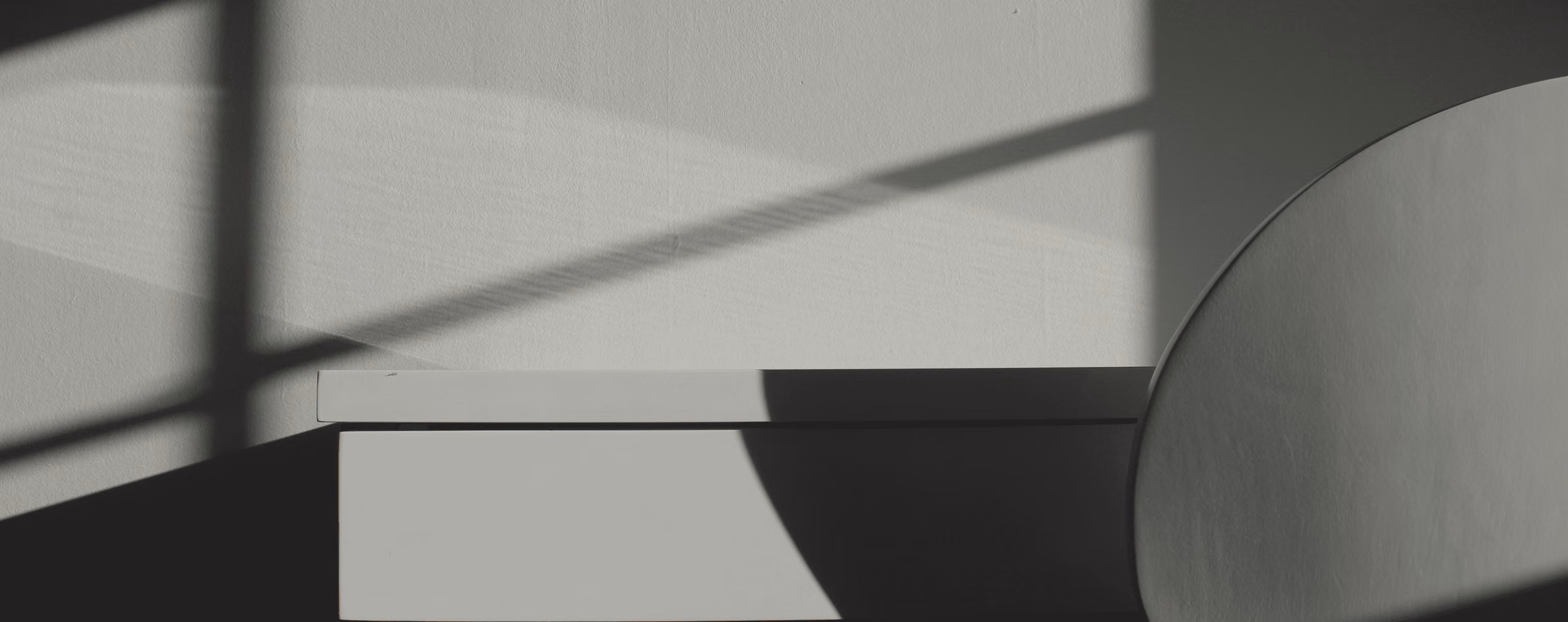 Black and white abstract photo showing shadows of window panes and a chair on a wall and desk.