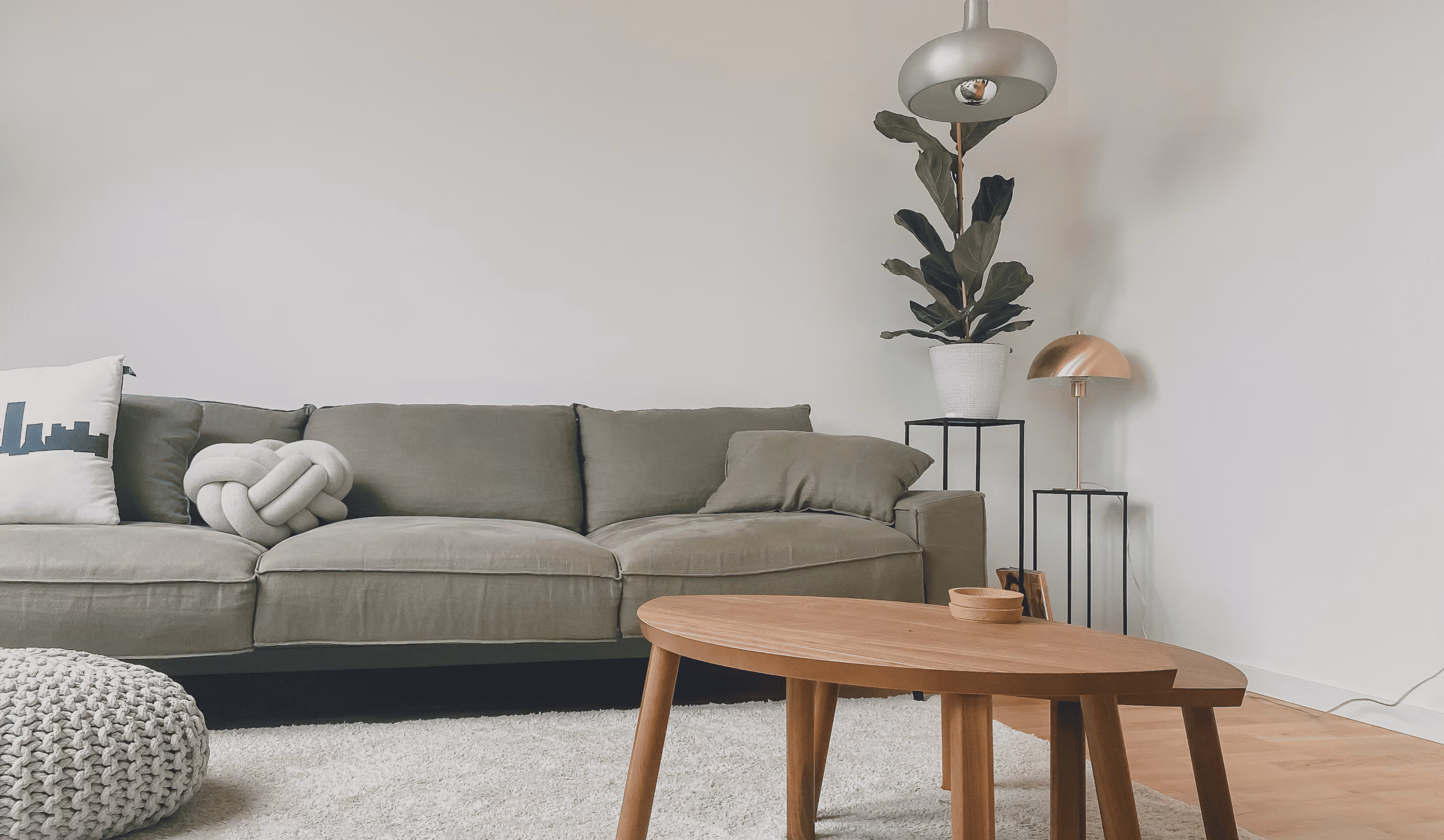 Modern living room with a green sofa, wooden coffee tables, knitted pouf, indoor plant, and lamps.