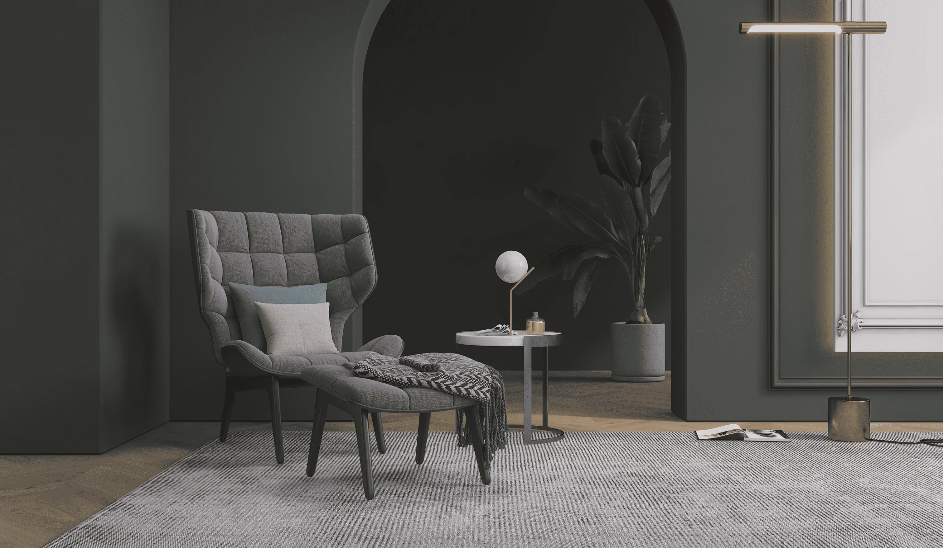 Gray modern armchair with cushions, side table, lamp, and potted plant in a dark moody room.