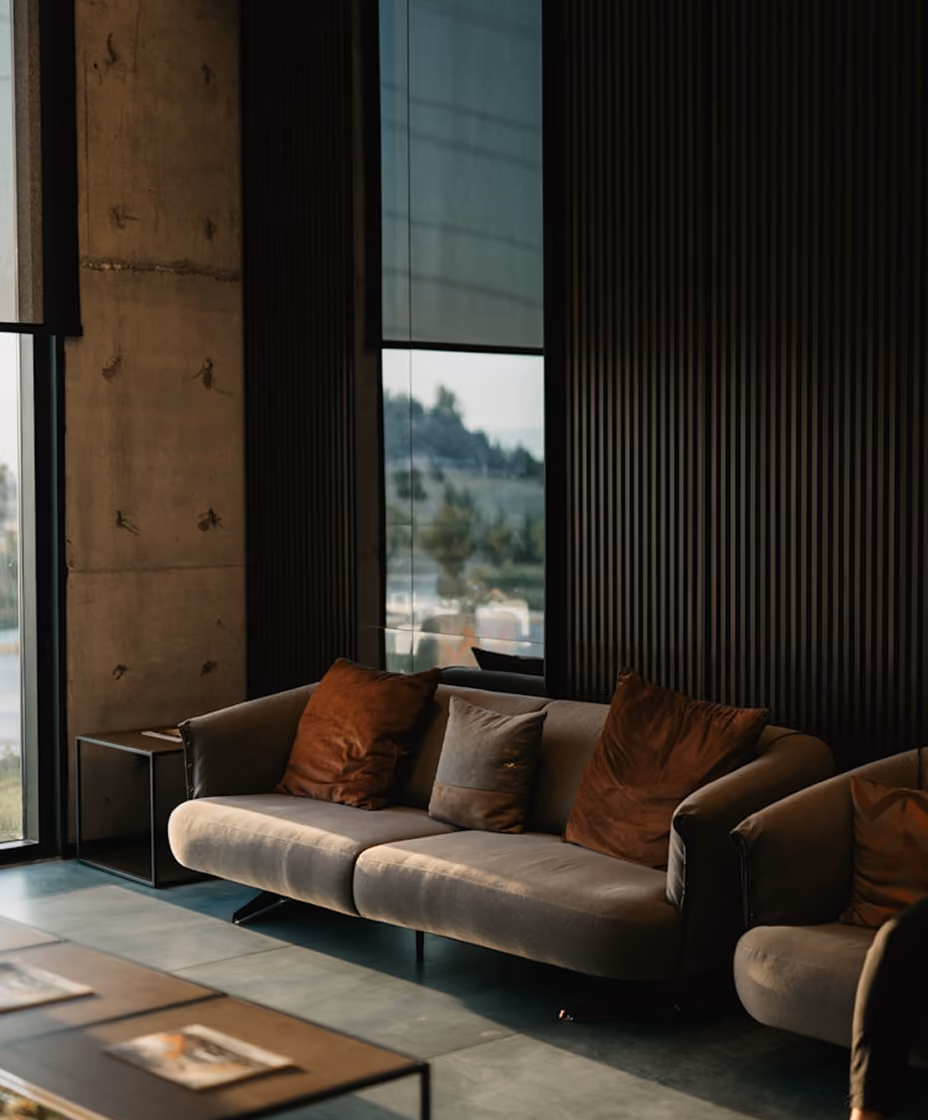 Modern living room with gray sofa, brown cushions, a small side table, and large windows.
