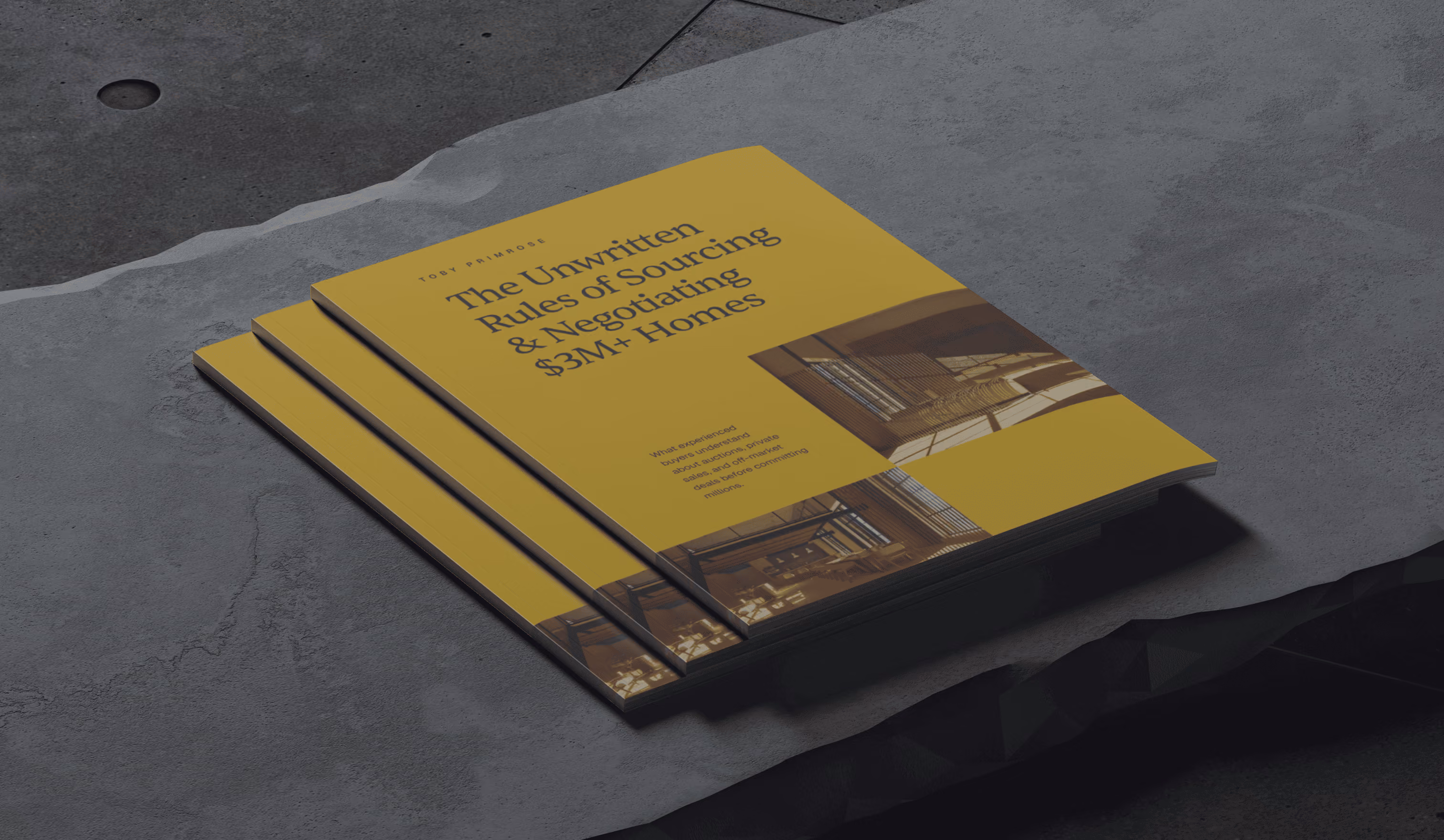 Stack of yellow books titled 'The Unwritten Rules of Sourcing & Negotiating $3M+ Homes' on stone surface.